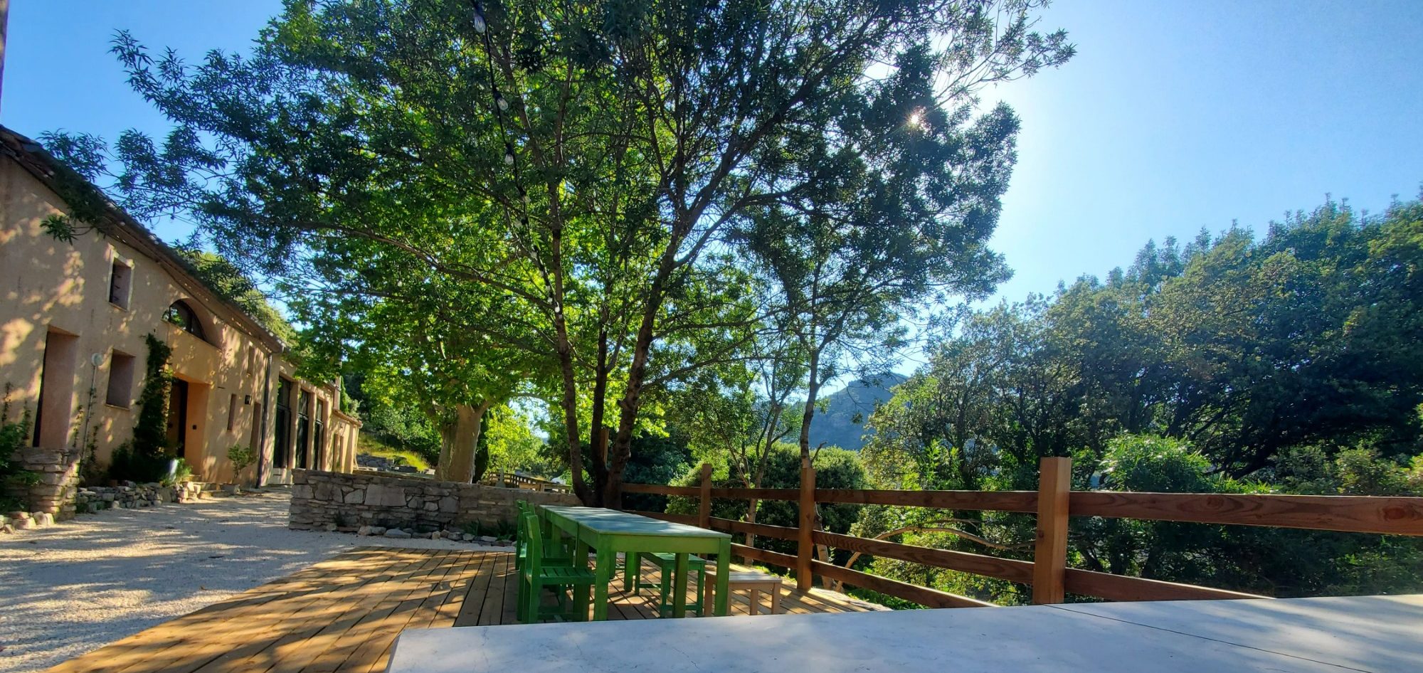 Vue d'une terrasse ombragée et une maison en arrière-plan sous un ciel bleu.